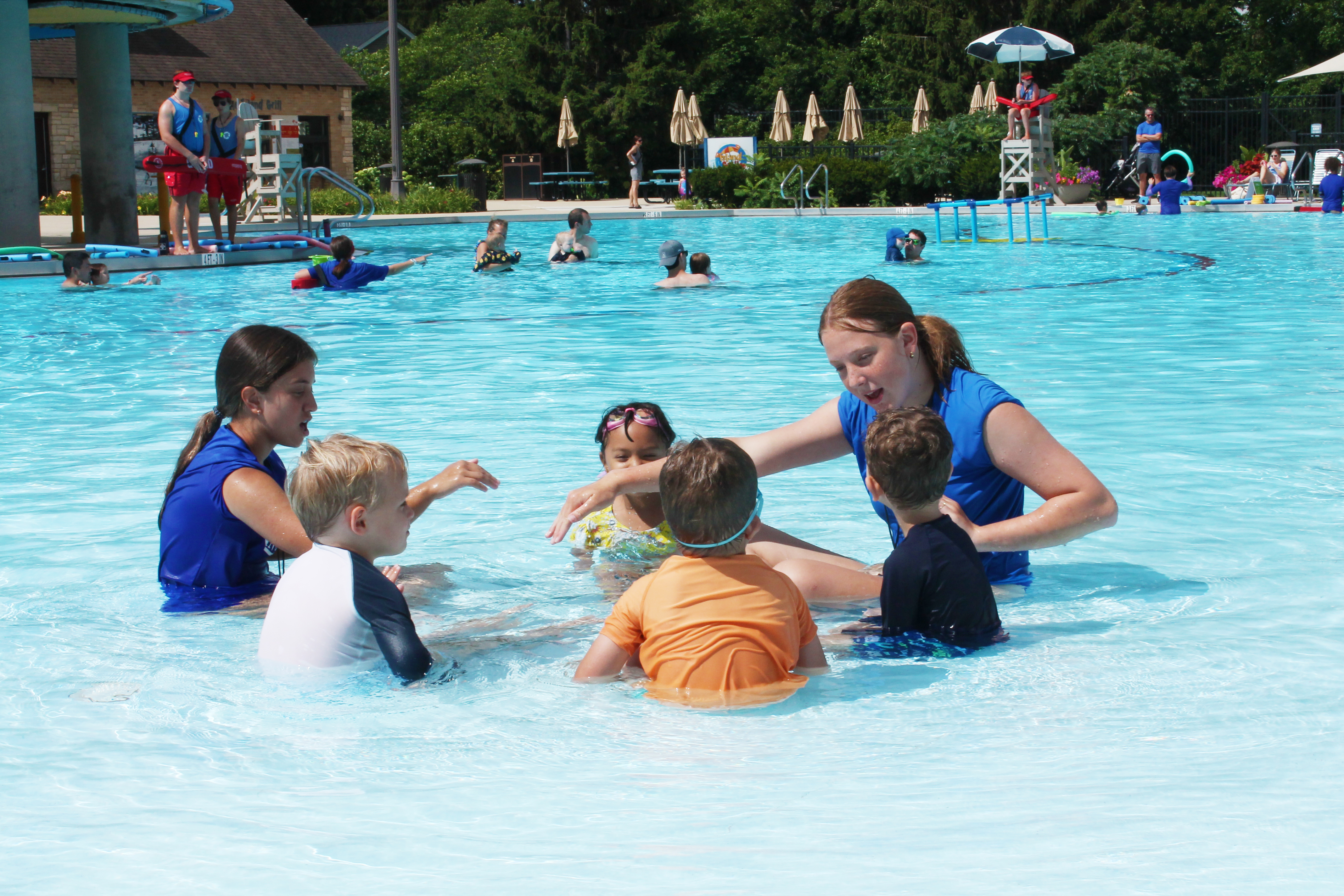 A circle of children sitting in the water with their swim instructor